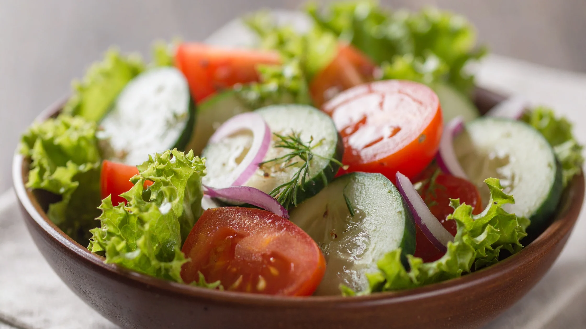 Fresh garden salad with sliced tomatoes, cucumbers, red onions, and lettuce in a bowl.