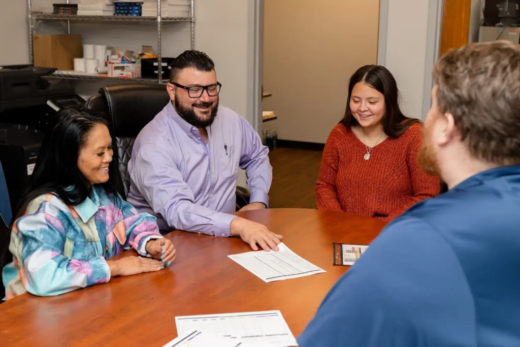 Four people meeting around a wooden conference table to review paperwork in an office setting.